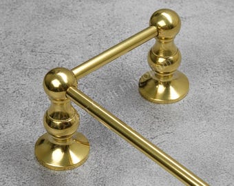 May include: A gold-colored towel rack with a classic design. The rack features two upright supports with decorative detailing and a horizontal bar for hanging towels. The finish is shiny and reflective, adding a touch of elegance to any bathroom.