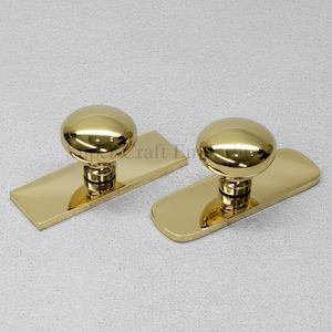 May include: Two gold-colored cabinet knobs with a round top and a rectangular base. The knobs are highly reflective, with a polished finish. The hardware is designed for furniture and home decor.