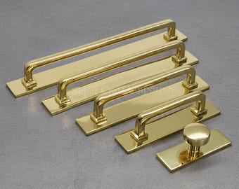 May include: A collection of gold-colored cabinet hardware, including several rectangular bar pulls and a round knob. The hardware is arranged on a gray surface, showcasing the variety of sizes and styles available for home decor projects.