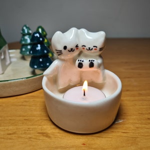 Pu&ograve; includere: Portacandele in ceramica bianca con due gatti carini che tengono una piccola candela. I gatti hanno occhi e bocca neri e tengono una piccola candela da t&egrave; bianca.