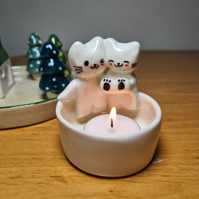 Pu&ograve; includere: Portacandele in ceramica bianca con due gatti carini che tengono una piccola candela. I gatti hanno occhi e bocca neri e tengono una piccola candela da t&egrave; bianca.