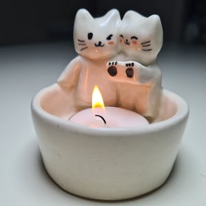 Pu&ograve; includere: Portacandele in ceramica bianca con due graziose figurine di gatti. Il portacandele contiene una piccola candela da t&egrave;.