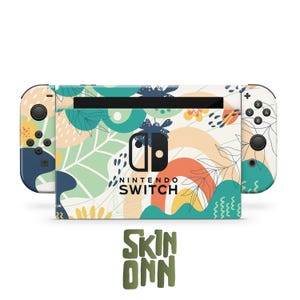 Puede incluir: Una consola Nintendo Switch con un diseño floral. Los mandos Joy-Con y el cuerpo de la consola están cubiertos con un patrón de hojas verdes, flores naranjas y amarillas y detalles azules sobre un fondo crema. El texto "NINTENDO SWITCH" es visible.
