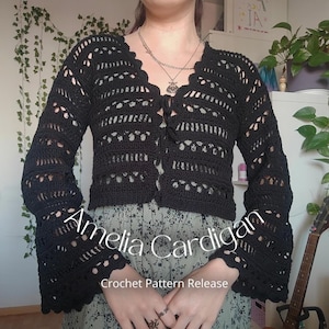 Könnte beinhalten: Eine schwarze Häkeljacke mit langen Glockenärmeln, einem geschwungenen V-Ausschnitt und einer Bindung vorne. Das Kleidungsstück zeigt ein komplexes Lochmuster. Der Text auf dem Bild lautet: Amelia Cardigan Crochet Pattern Release.