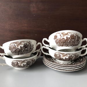 May include: A collection of vintage white ceramic soup bowls and saucers with a brown transferware design. The bowls have two handles and the saucers are stacked. The transferware depicts a rural scene.