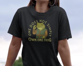 May include: Black t-shirt with a humorous graphic featuring a frog in a vest and the text "ONE DOES NOT SIMPLY OWN ONE FROG" in a circular design. The frog is green and the text is in gold.
