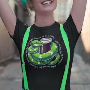 May include: Black t-shirt featuring a green snake wrapped around a glass of beer. The text on the shirt reads "Snakes are back for St. Paddy's!"