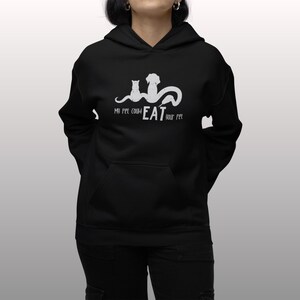 Op de afbeelding: Zwarte hoodie met een witte afbeelding van een kat en een hond met de tekst "Mijn huisdier zou jouw huisdier kunnen opeten."