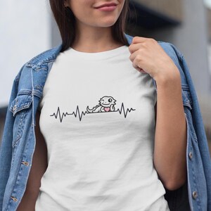May include: White t-shirt featuring a black and white illustration of a bearded dragon holding a pink heart. The illustration is on a heartbeat line. The text "I love bearded dragons" is not visible in the image.