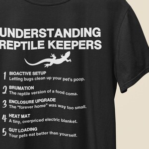 May include: Black t-shirt with white text: "UNDERSTANDING REPTILE KEEPERS" and a lizard graphic. The shirt humorously details reptile care, including bioactive setups, brumation, enclosure upgrades, heat mats, and gut loading.