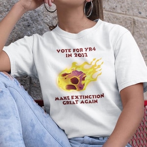 May include: White t-shirt with a graphic of a flaming asteroid and the text "Vote for Yr4 in 2032" and "Make Extinction Great Again".