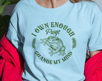 May include: Light blue t-shirt with the text "I OWN ENOUGH Frogs CHANGE MY MIND" in green, surrounding a green frog illustration. The shirt is a solid color and has short sleeves.