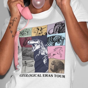 May include: White t-shirt with a grid of colourful illustrations of prehistoric creatures. The design includes a Tyrannosaurus Rex, a woolly mammoth, and the text "GEOLOGICAL ERAS TOUR".