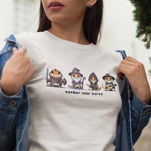May include: White t-shirt featuring a graphic of five cartoon bearded dragons dressed as fantasy characters. The text "gather your party" is printed below the characters.