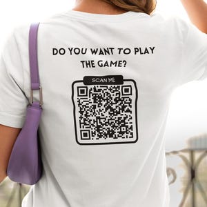 May include: White t-shirt with the text "Do you want to play the game?" and a black and white QR code with the text "Scan Me" above it.