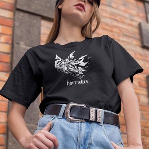 Pode incluir: Camiseta preta com um gráfico branco de um lagarto com chifres e a palavra "horridus" impressa abaixo da imagem.