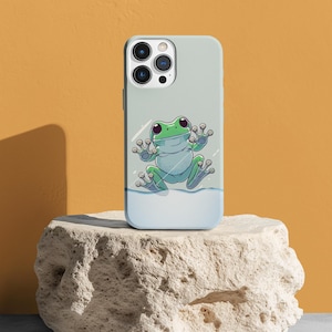 Puede incluir: Una funda de teléfono azul claro con una ilustración de rana verde. La rana se aferra al interior de la funda, como si intentara escapar. La funda del teléfono tiene un recorte para el objetivo de la cámara y un fondo blanco.