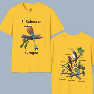 May include: Two yellow t-shirts with Central American bird and country names printed on them. The front shirt features a blue and green bird called a "Torogoz" with the text "El Salvador". The back shirt features a tree branch with various birds and the names of Central American countries: Panama, Honduras, Guatemala, Belize, El Salvador, Costa Rica, and Nicaragua.