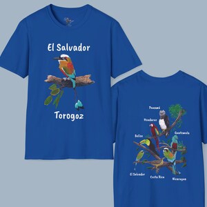 May include: Two royal blue t-shirts with a bird and text on the front and a bird design on the back. The front of the left shirt features a colorful bird with the text "El Salvador Torogoz". The back of the right shirt features a design of birds with the names of Central American countries: Panama, Honduras, Belize, Guatemala, El Salvador, Costa Rica, and Nicaragua.
