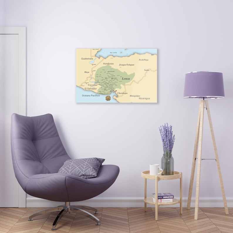 May include: A map of Central America with a green area highlighting the Lenca region. The map is printed on a beige background and framed in a light wood frame. The map is hanging on a white wall above a purple armchair and a small wooden side table.
