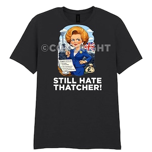 Puede incluir: Camiseta negra con una ilustración de dibujos animados de una mujer con un traje azul, sosteniendo una lista y una bandera de la Union Jack. El texto "STILL HATE THATCHER!" está impreso debajo.