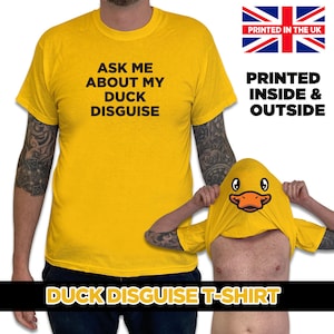 May include: A yellow t-shirt with the text "Ask me about my duck disguise" printed on the front. The t-shirt is being worn by a person with tattoos on their arms. The t-shirt is also being worn by a person with their head inside the shirt, revealing a duck face printed on the inside of the shirt.