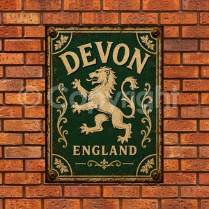 May include: A rectangular metal sign with a dark green background and a distressed finish. The sign features the text DEVON at the top and ENGLAND at the bottom in a cream-coloured font, with a central illustration of a rampant lion.