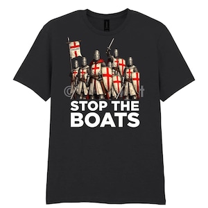 Peut inclure: T-shirt noir avec un motif de chevaliers médiévaux en armure, tenant des épées et des boucliers, et un drapeau avec "England". Le texte "STOP THE BOATS" est imprimé en blanc en dessous.