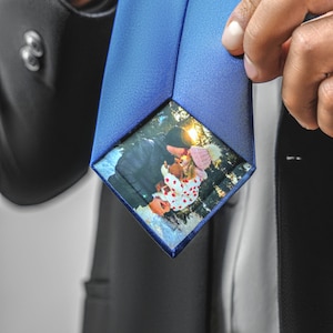 Könnte beinhalten: Eine blaue Seidenkrawatte mit einem Foto eines Paares, das sich in einer verschneiten Waldszene küsst. Das Foto ist quadratisch und mittig auf der Krawatte platziert.