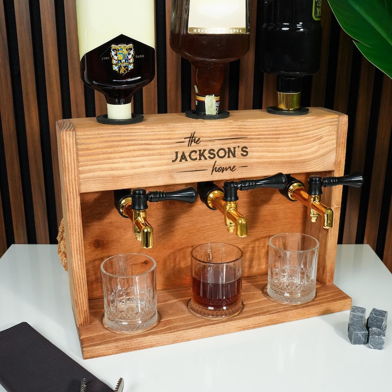 A wooden dispenser with three glass taps, each containing a different type of liquor, arranged on a white table.