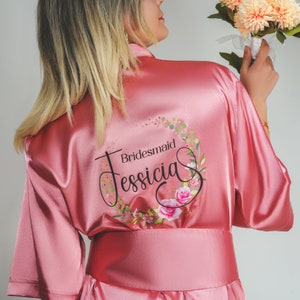 Pode incluir: Roupão de cetim rosa com um design de coroa de flores e o texto "Bridemaid Jessica".