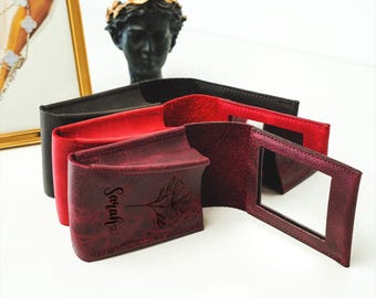 May include: Three small, rectangular, leather-bound cases with mirrors. The case on the right is open, revealing a mirror. The case in the middle is burgundy and has the name "Sarah" engraved on it. The case on the left is black.