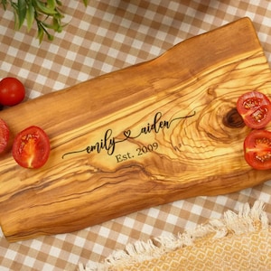 Könnte beinhalten: Holzschneidebrett mit natürlicher Maserung. Auf dem Brett sind die Namen "emily & aiden" mit einem Herzsymbol und dem Jahr "Est. 2009" in Schwarz eingraviert. Rote Kirschtomaten sind um das Brett herum angeordnet.