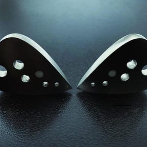 May include: Two silver guitar picks with multiple circular cutouts. The picks are shaped like a teardrop and have a smooth, metallic finish.