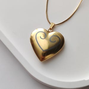 May include: A gold heart-shaped locket necklace with a black swirl design on the front.
