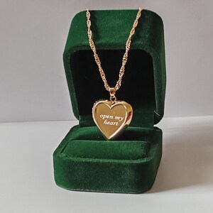 Könnte beinhalten: Goldfarbene herzförmige Halskette mit dem Schriftzug "open my heart". Die Halskette wird in einer dunkelgrünen Samt-Schmuckschatulle präsentiert. Die Kette hat ein gedrehtes Seil-Design.