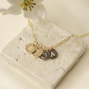 May include: Gold necklace with multiple small round charms, each with a letter engraved on it. The charms are attached to a delicate gold chain.