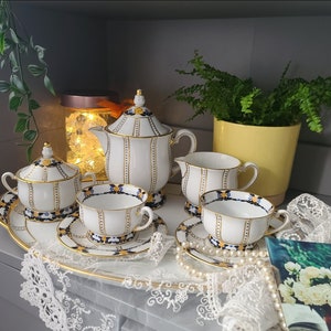 May include: A white tea set with blue and gold accents. The set includes a teapot, creamer, sugar bowl, and four teacups and saucers. The teacups and saucers have a floral pattern.