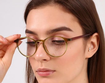 May include: A woman wearing round, green-framed eyeglasses with a brown temple.