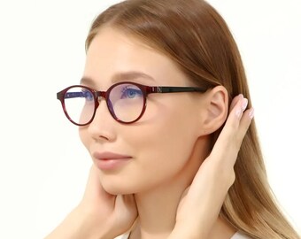 Könnte beinhalten: Runde Brille mit bordeauxfarbenem Rahmen und schwarzen Bügeln. Die Brille hat klare Gläser. Der Hintergrund ist weiß.