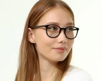 May include: A woman wearing black framed eyeglasses with clear lenses. She has long, straight, light brown hair and is wearing a white t-shirt.