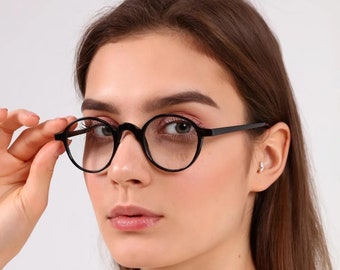 May include: A woman wearing black round glasses with a white shirt.
