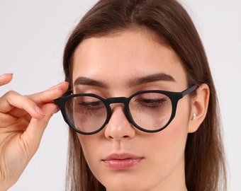 May include: A woman wearing black round eyeglasses with a white shirt.