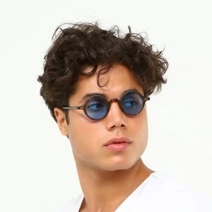 May include: Round sunglasses with brown frames and blue lenses. The glasses have a classic design with a thin metal bridge and temples. The lenses are a vibrant blue color, and the frames are a tortoiseshell pattern.