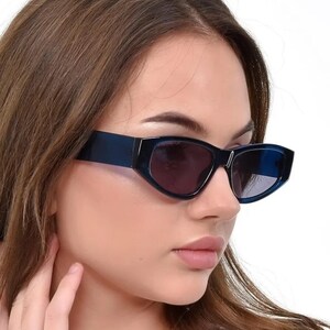 May include: A woman wearing blue cat-eye sunglasses with a dark blue frame and dark lenses. The sunglasses have a slight gradient effect on the lenses.