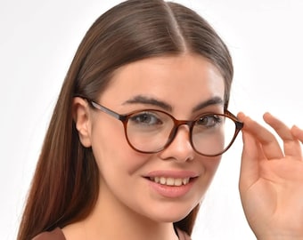 Könnte beinhalten: Eine Frau trägt eine runde Brille aus braunem Schildpatt mit einem braunen T-Shirt.