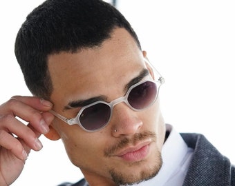 May include: A man wearing a white shirt and a dark gray blazer with a textured pattern. He is wearing clear framed sunglasses with dark lenses.