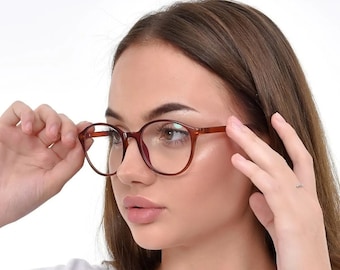 Könnte beinhalten: Eine Frau trägt eine runde braune Brille mit einem weißen T-Shirt.