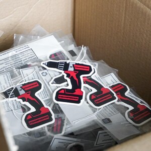 K&ouml;nnte beinhalten: Eine Schachtel voller Aufkleber mit einem rot-schwarzen Bohrmaschinendesign. Die Aufkleber tragen die Aufschrift "#TRADEFRESHUK" und "TRADEFRESHUK". Die Aufkleber sind in durchsichtigem Kunststoff verpackt.