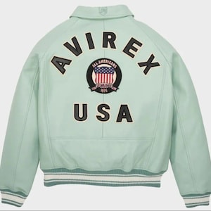 May include: A light green leather jacket with the word "AVIREX" arched across the back in black letters. Below the word "AVIREX" is a circular patch with the words "ALL AMERICANS" and "ESTABLISHED 1975" surrounding a graphic of the American flag. The word "USA" is below the patch.